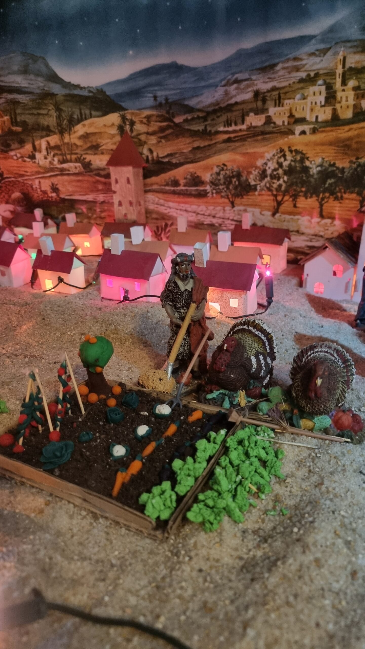 Huerto creado con plastilina y, al fondo, un pueblo andaluz con casas blancas y tejados a dos aguas recreado en el belén.