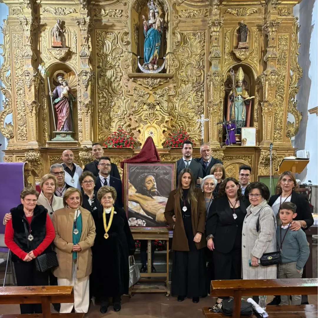 Foto de familia tras la presentación del cartel anunciador de la Semana Santa 2026 de Peligros, con miembros de la Hermandad y asistentes al acto, en el altar mayor de la Iglesia Parroquial de San Ildefonso.