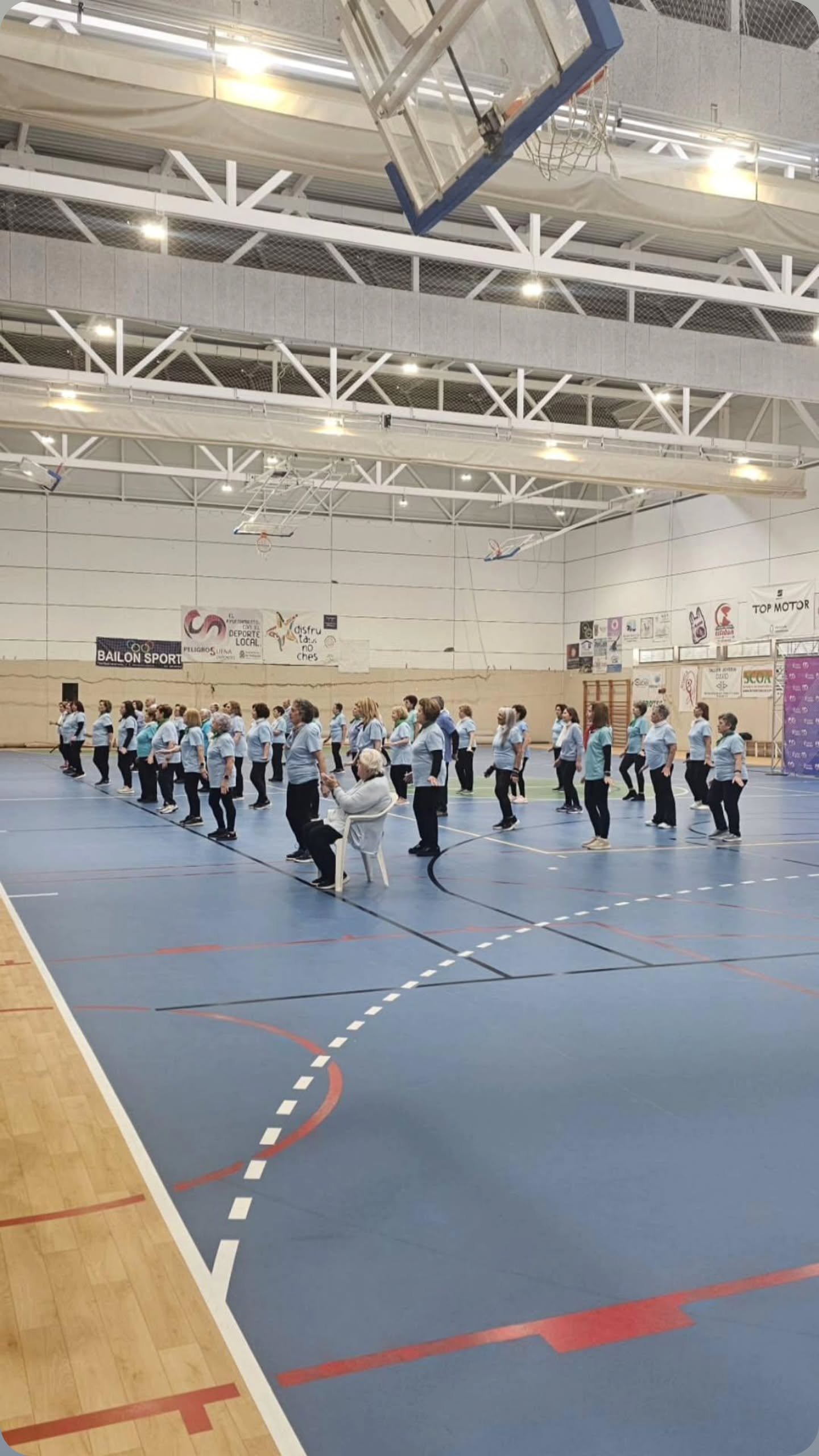 Participantes en una actividad física dirigida ocupando la pista del pabellón municipal.